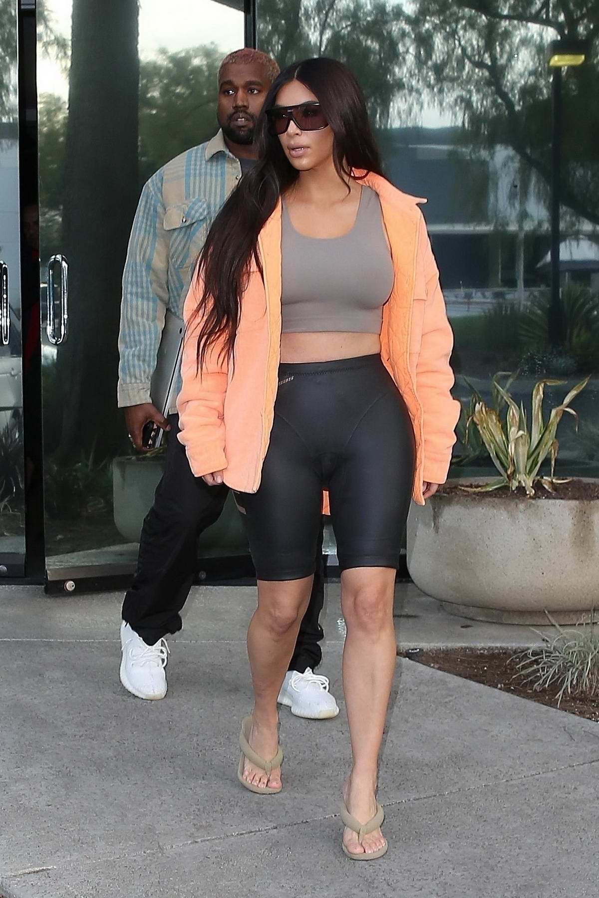 Kim Kardashian wears an orange jacket over a cropped vest top with ...