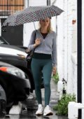 Margot Robbie wears a cropped grey jacket and green leggings as she arrives at the gym holding an umbrella in Los Angeles