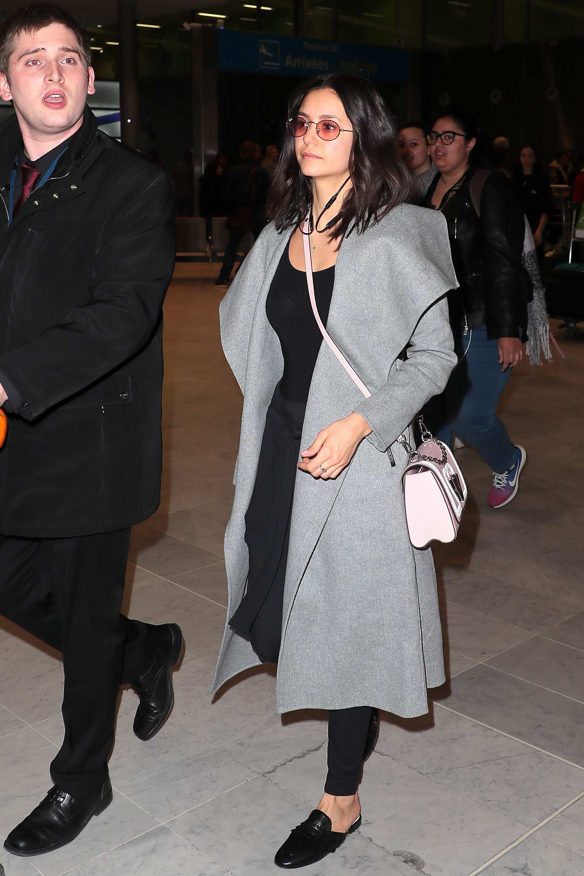 nina dobrev looks casual yet trendy in a grey long coat paired with a black outfit and pink ...