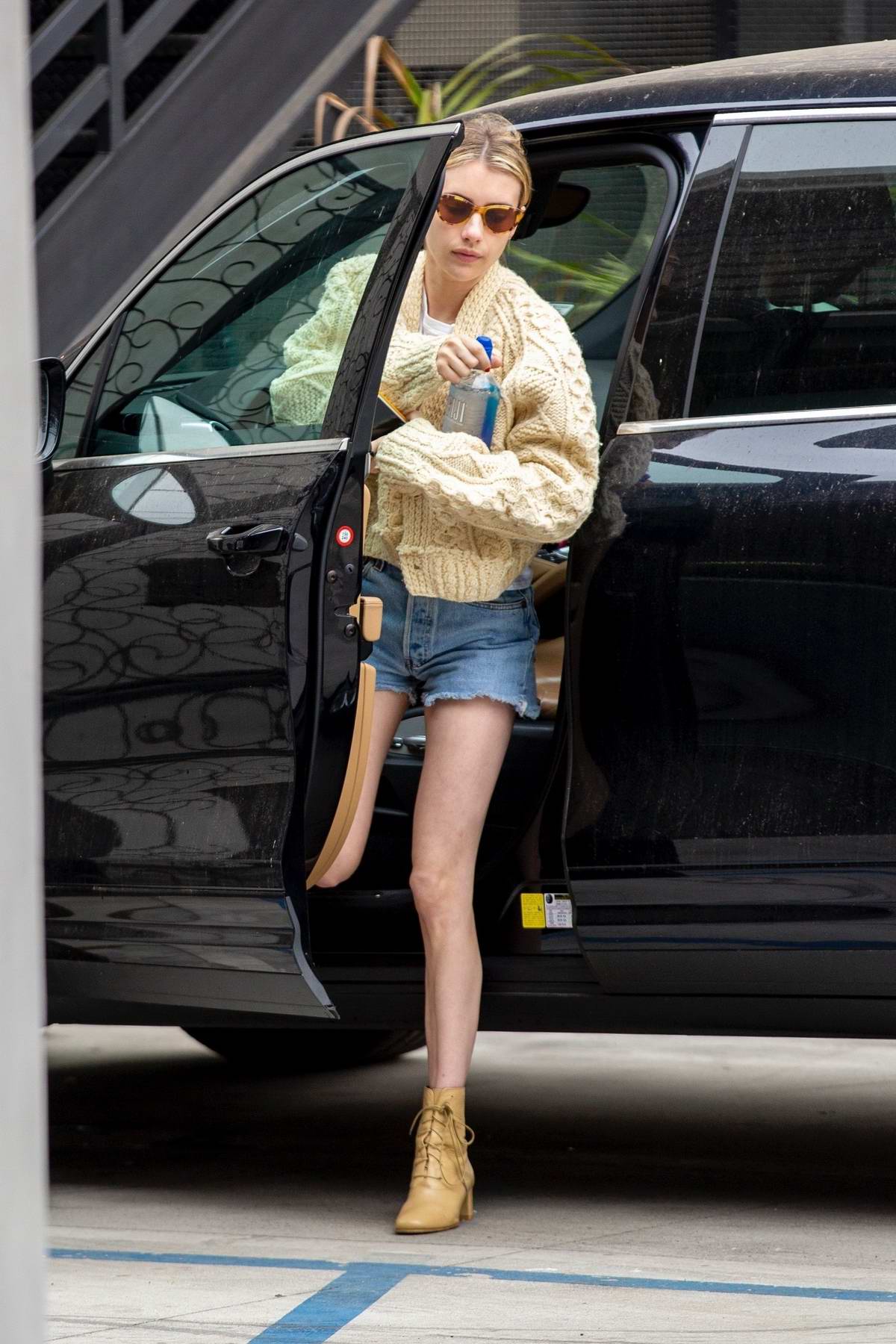 Emma Roberts wears a knitted yellow cardigan and denim shorts