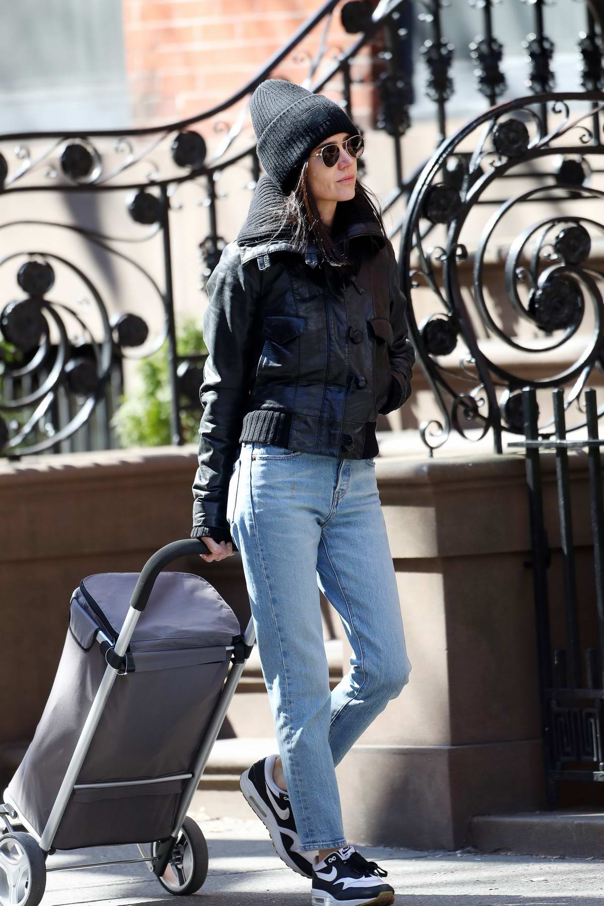 Jennifer Connelly bundles up in a black beanie, matching jacket, jeans, and  Nike trainer while out
