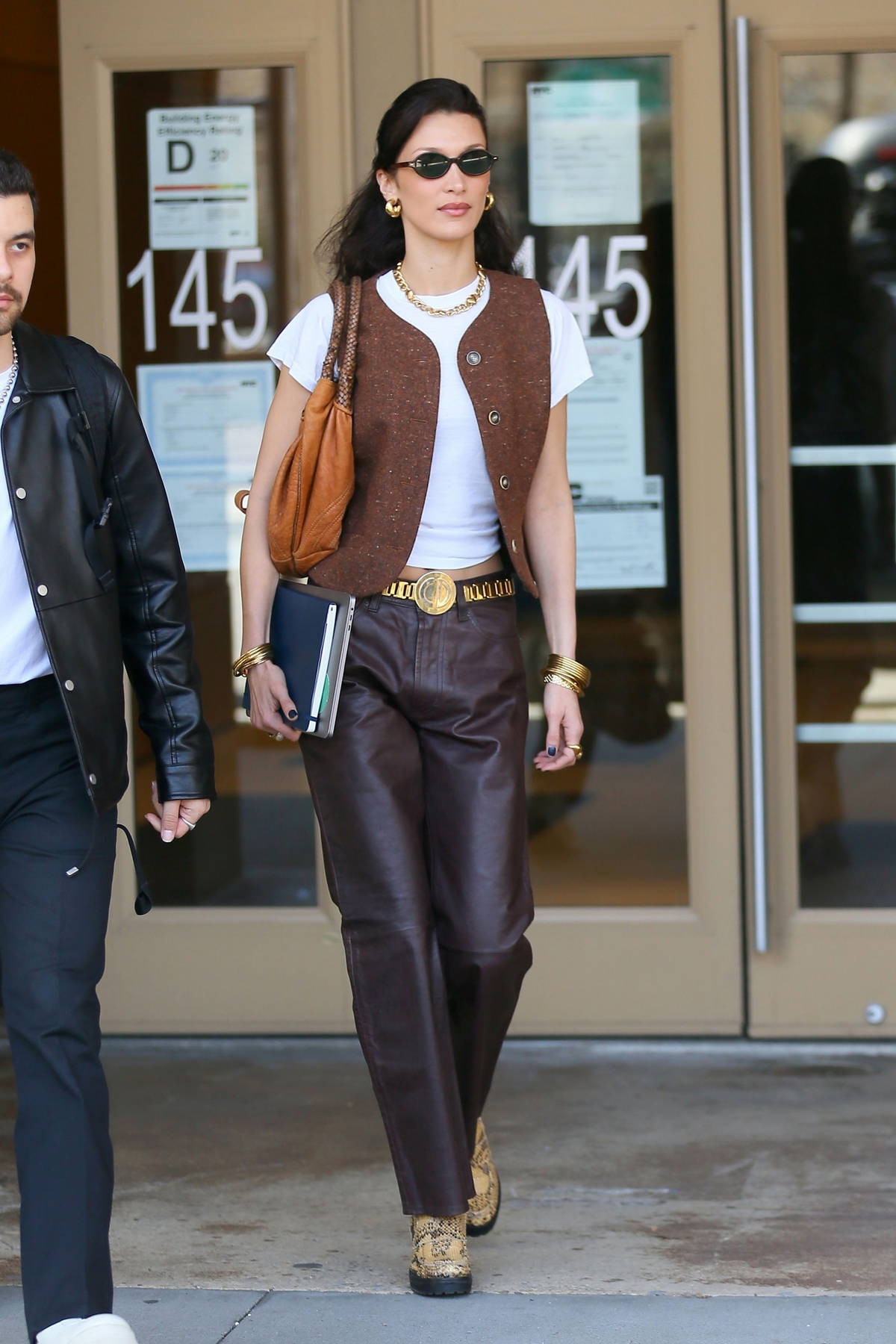 Bella Hadid looks stylish in a brown suede vest, brown leather pants and  snakeskin boots as