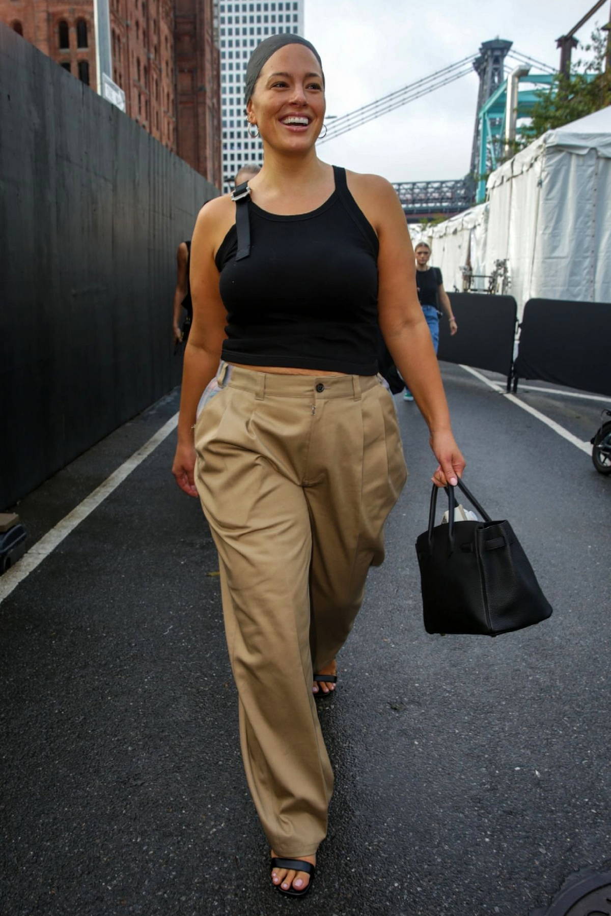 Ashley Graham slips into a black tank top and pleated khaki slacks when  leaving the Michael Kors fashion show where she modeled an elegant dress