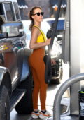 Maggie Q displays her fit physique in a yellow sports bra and orange leggings while stopping at a gas station in Los Angeles